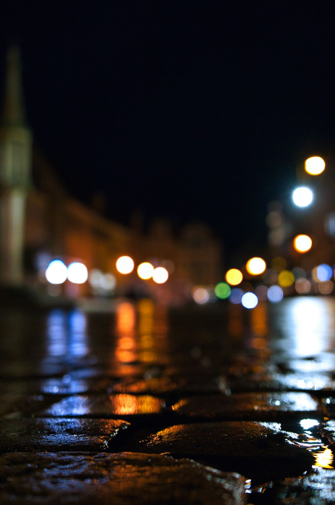 Rainy cobblestone street at night with warm streetlights